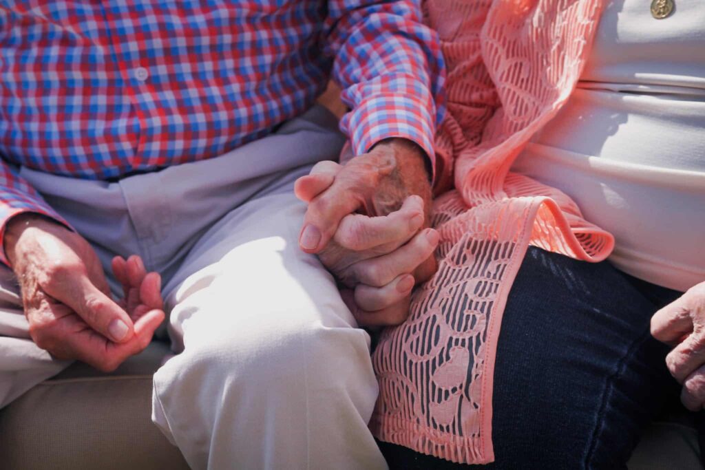 Crop unrecognizable aged couple in casual clothes sitting close and holding hands while spending time together